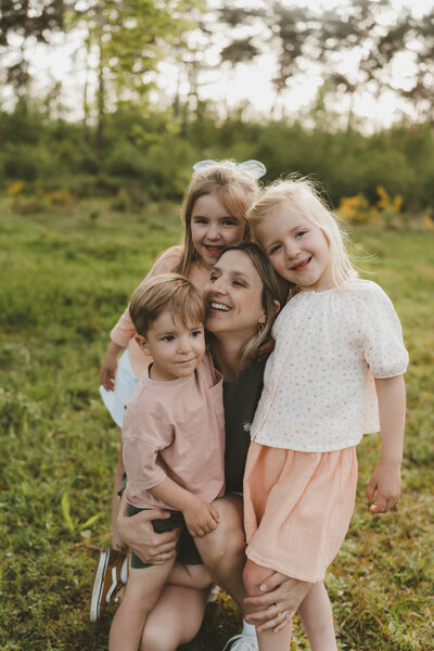 Moeder met haar drie kinderen op de schoot in een veld met bloemen,.