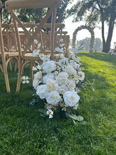 A wedding ceremony setup featuring, a silk floral arrangement of white roses and greenery. Representing Sylk Floral Studio's vendor profile for the Crush Collective wedding show.
