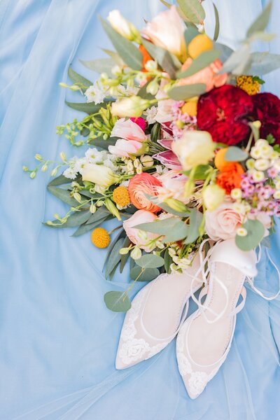 lace wedding shoes and colorful bouquet on a blue background