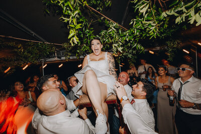 Wedding guests raising bride up on a chair during wedding reception