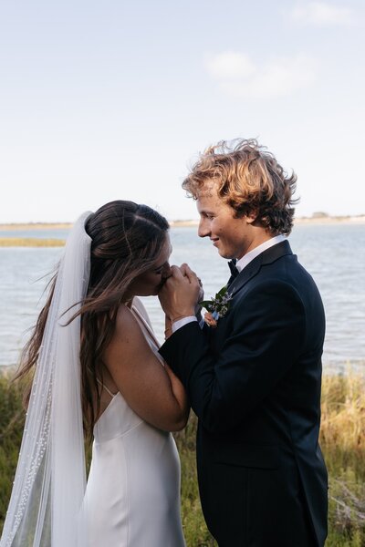 indie west portfolio image of bride kissing grooms hand next to beach