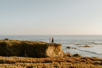 bride and groom running on beach cliff