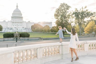 A mother walks her daughter along a marble fence outside the US Capitol Building photographed by Family Photographer Northern Virginia Marie Elizabeth Photography