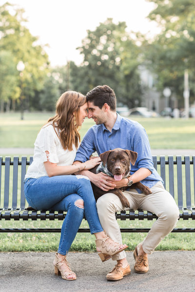 couple holding their chocolate lab sitting on a bench