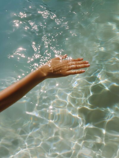 Hand gently skims the top of crystal clear ocean water