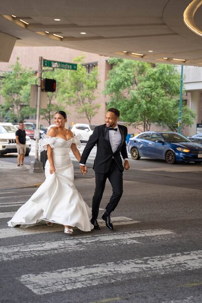 Bride and groom running hand in hand across Washington Street after downtown Indianapolis Artsgarden wedding ceremony