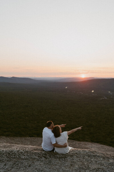 Couple sitting together on the summit of North Sugarloaf Mountain in the White Mountains of New Hampshire at sunset.