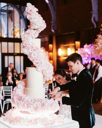 Grand six tier wedding cake with four edible tiers and two illusion floating spacer tiers in ivory buttercream with a beautiful cascade of cherry blossom spiralling from top to bottom
