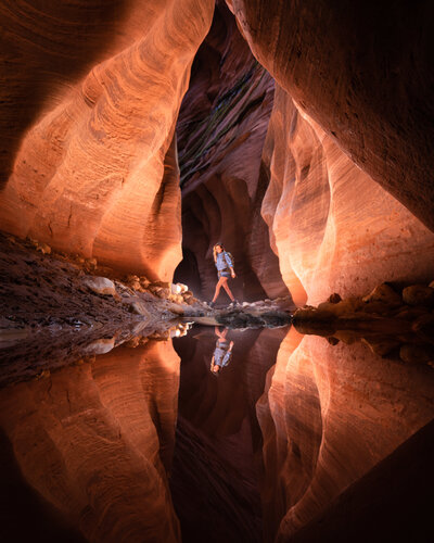 Woman standing inside an orange colored canyon with a reflection in the water