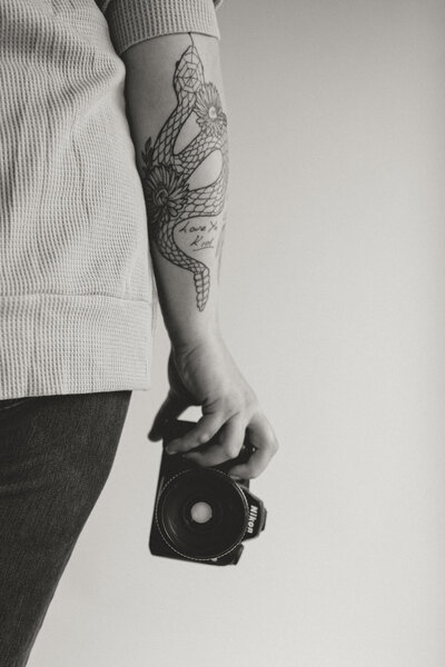 Black and white image of a tattooed arm holding a nikon camera