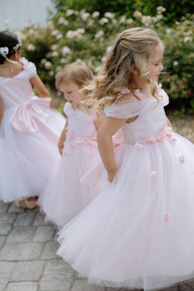 Three flower girls twirl around in their pink dresses