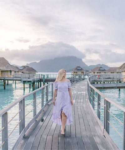 Woman walking on dock toward overwater bungalows in tropical mountain setting