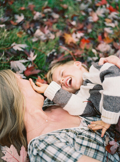 Mother and son rolling in a pile of leaves and giggling taken by Little Rock photographer Bailey Feeler