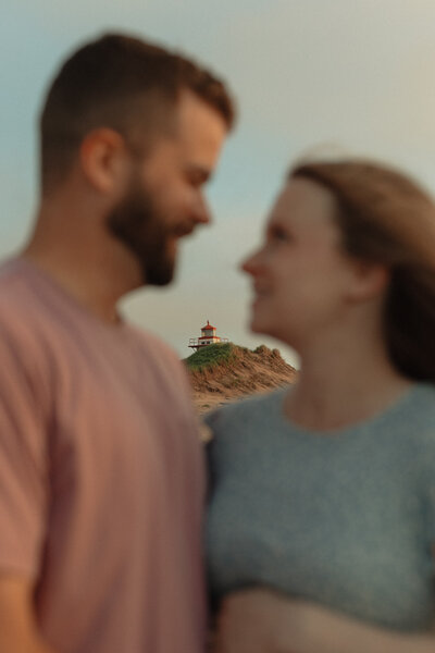 couple embrace in front of light house for lifestyle photos in prince edward island