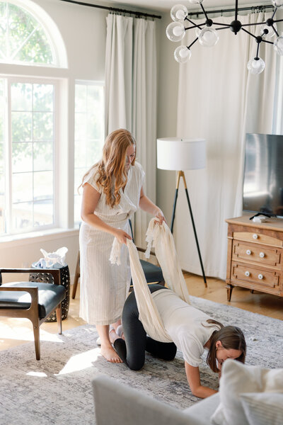 Amanda of Fleuritage offering gentle birth support with a rebozo in a warm, sunlit living room.