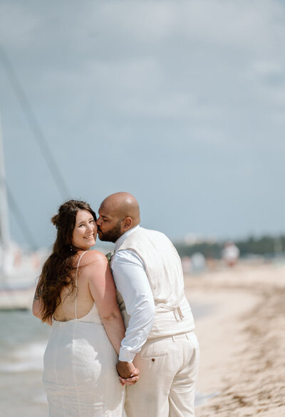 A couple by the beach kisses near a boat at their wedding in Cozumel