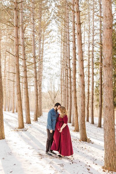 Winter maternity photoshoot at Retzer Nature Center in Waukesha, Wisconsin. Couple nose to nose in pine trees.
