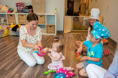 Blonde woman teaching a kids entertainment and music class, while dressing up as chefs and pretend cooking.