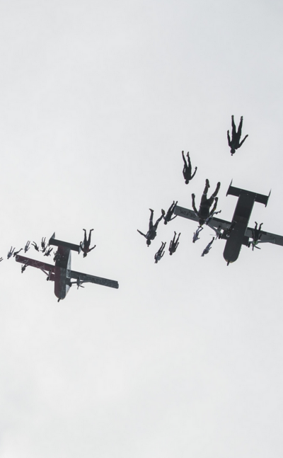 Das Bild zeigt Fallschirmspringer, die aus zwei Pink Skyvans in Formation springen