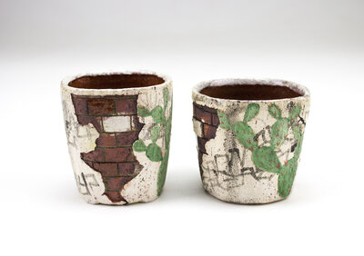 A ceramic cup that resembles plaster falling apart from red bricks with painted cacti and graffiti