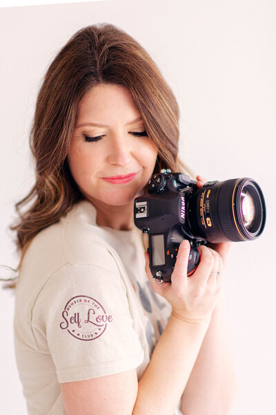 Kalee holding camera with Self Love Club shirt.
