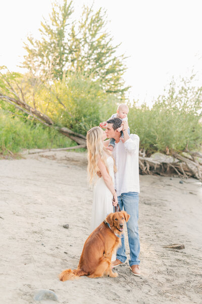  a family of three posing on the beach for their Lewiston, Idaho family lifestyle, photo shoot, with their golden retriever puppy
