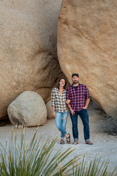 Two adventure elopement photographers standing together in a desert landscape with large rock formations, capturing their love for the outdoors and exploration.
