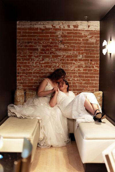A newlywed couple laying on a couch together as one kisses the other's forehead.