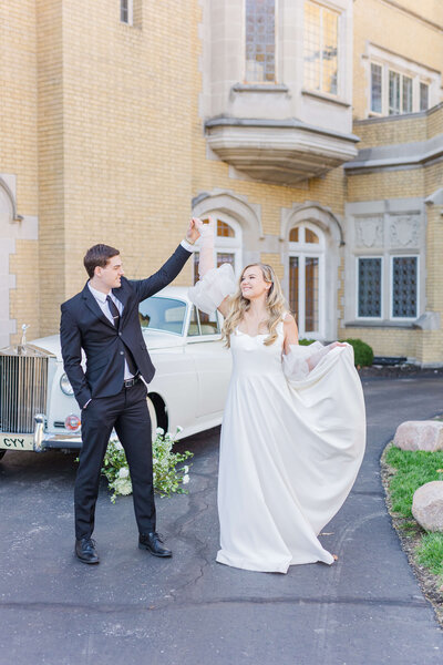 A groom twirls the bride in front of a rolls royce.