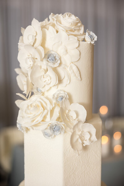 white wedding cake with ornate white florals on top and cascading along the side