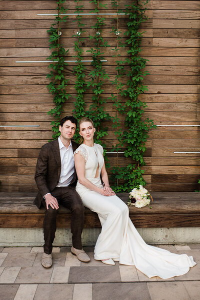 bride and groom sitting on bench in front of ivy wall in Boston