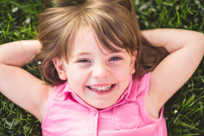 Little girl laughing with her arms behind her head and laying in the grass.  Photo by Dripping Springs Texas based Lydia Teague Photography.