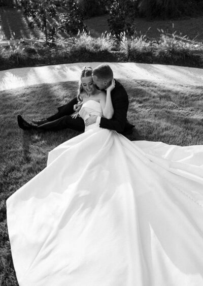 bride is laying down on her groom in the grass with her dress flowing out 