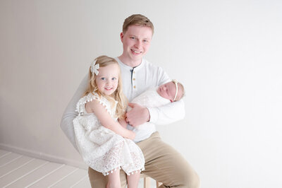 Dad holding newborn and toddler in studio 