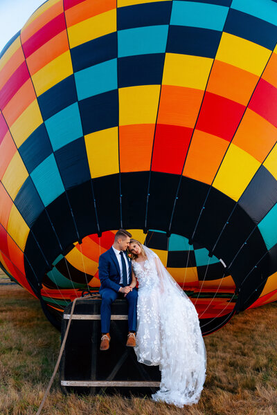A bride and groom sitting in front of a colorful hot air balloon, captured by an Oregon elopement photographer.