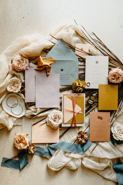 Flat lay of colorful wedding stationery and fresh flowers styled with ribbons, perfect for a Mexico destination wedding.