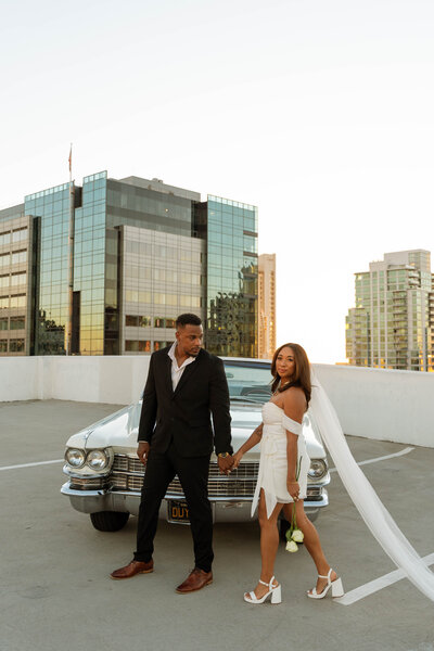 a man and woman engagement photos with a classic car on a rooftop garage