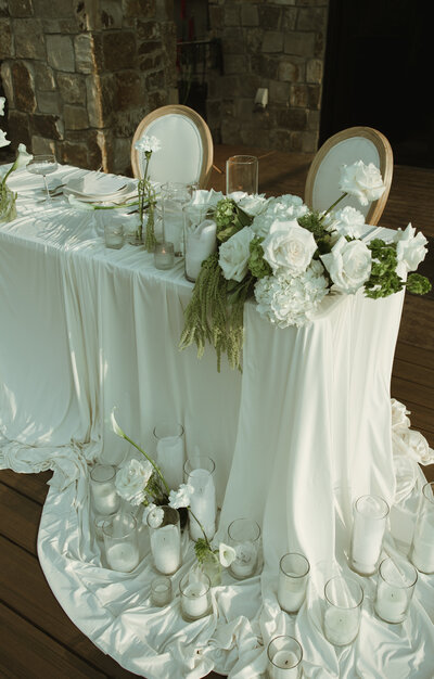 Bride and groom table with white florals, candles, and table cloths