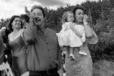 Mom and dad wipe eyes while toddler looks stoic at wedding