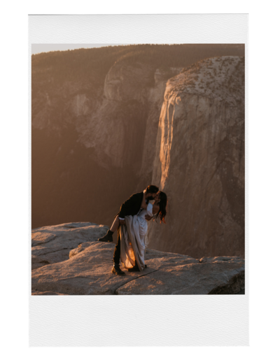 groom dips bride while they kiss standing on a rock cliff with el  capitan in the background there is a ray of orange sunlight hitting the rock behind them and the photo is in a polaroid frame