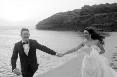 Black and white photo of a bride and groom running on a beach in Hawaii during their destination wedding.