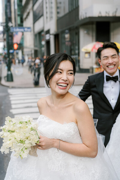 Laughing bride and groom with sweet pea bouquet on Fifth Ave in NYC