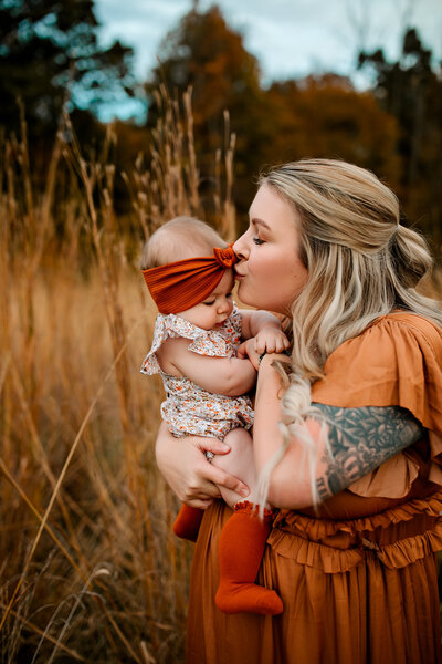 A mother kissing her six month old outdoors with Fall colors.