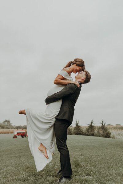 Groom lifts his bride in a field on their wedding day