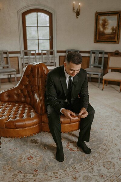 Groom in black tux reading love note at Chateau de Harpe