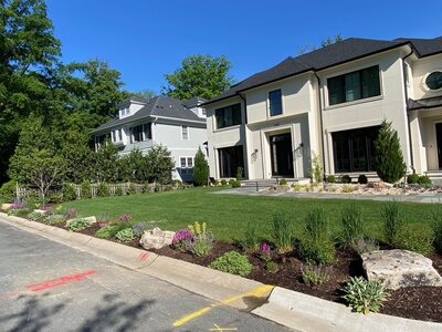 Completed luxury home with a beautifully landscaped front yard featuring lush green grass, a stone walkway, and vibrant plants along the curb.