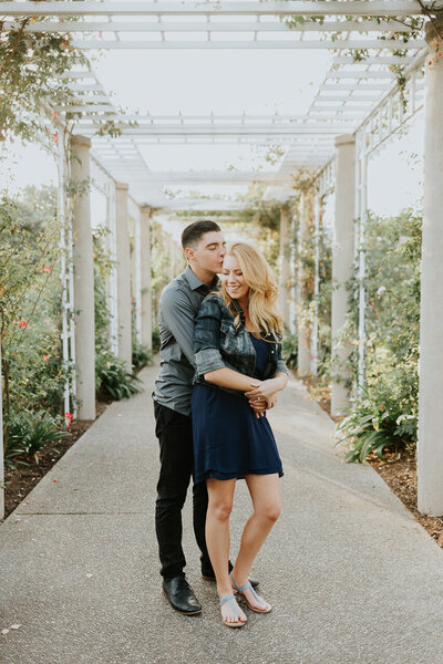 Two people are wapped up in each others arms in a walkway in a garden.