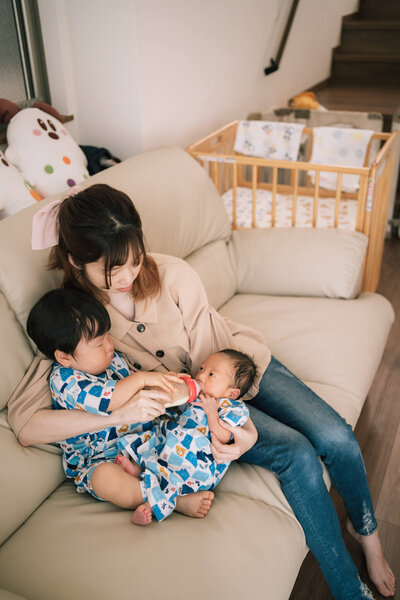 ソファで新生児にミルクをあげるママとお兄ちゃん