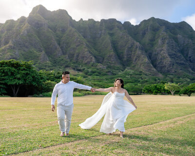 Asian couple bride and groom eloping at Oahu, Hawaii at Kualoa Regional Park with open field and mountains in the background.