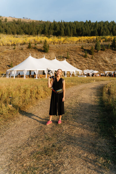 Jackson Hole micro wedding photographer standing outside holding her camera with wedding tent in the background
